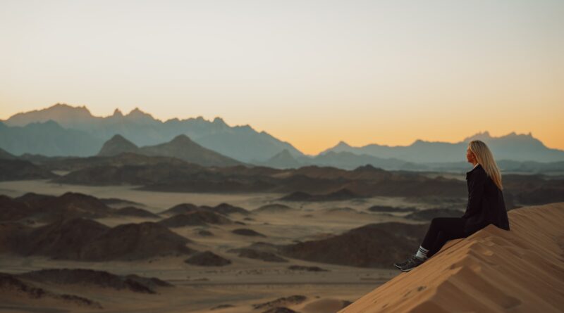 a woman sitting on top of a sand dune
